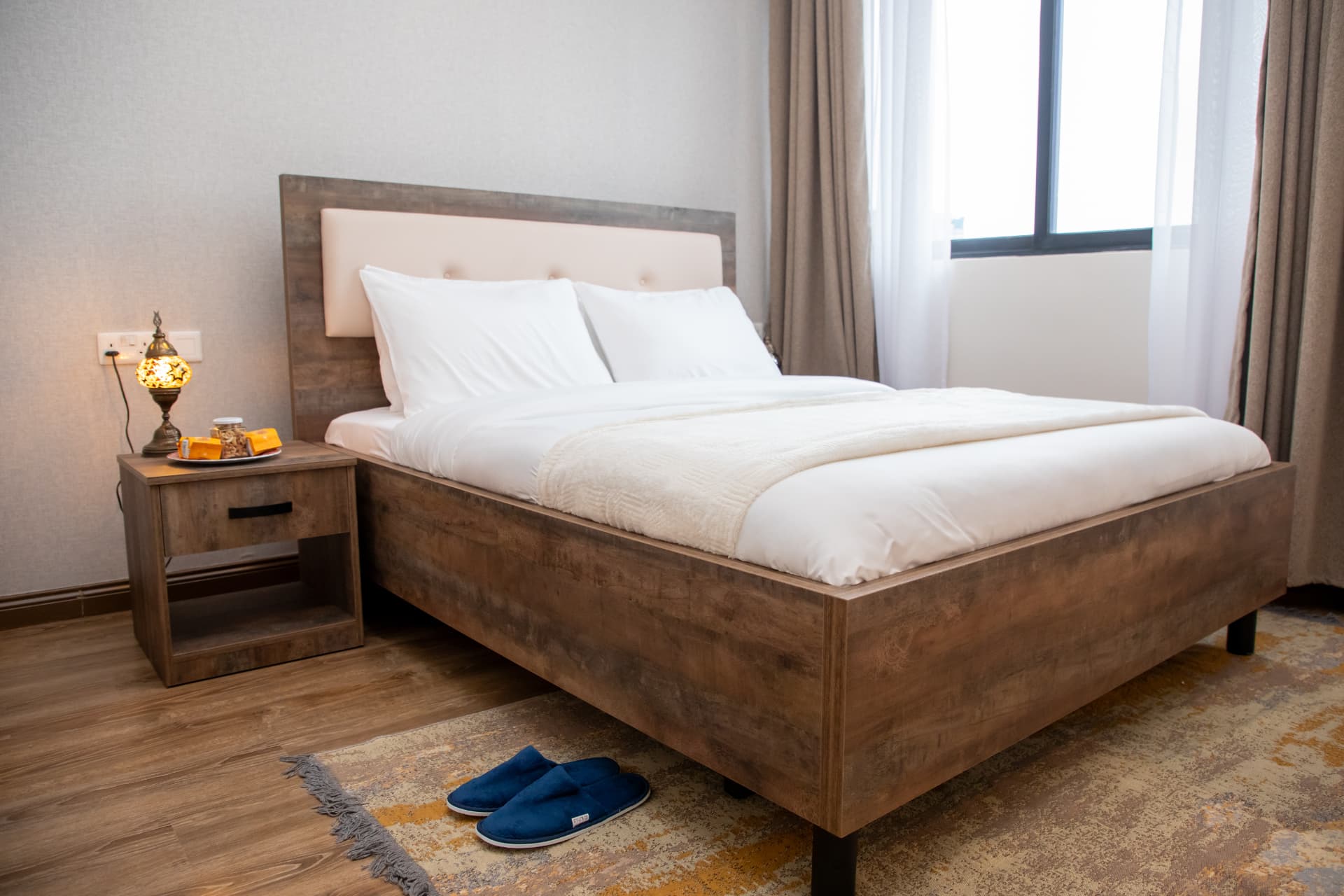 Wooden bed with white linens and slippers on the rug