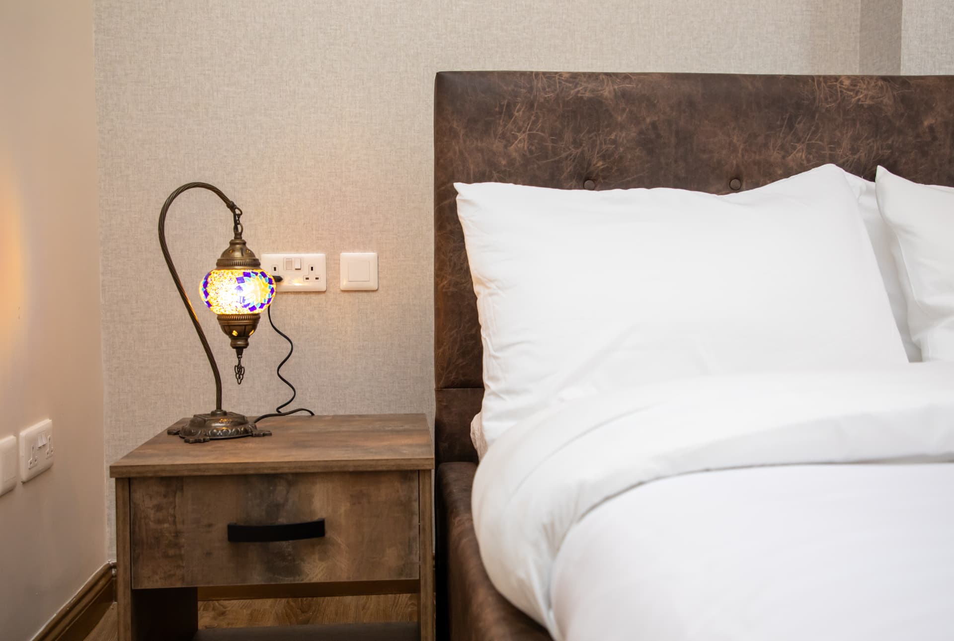 Bedside table with mosaic lamp beside crisp white pillows