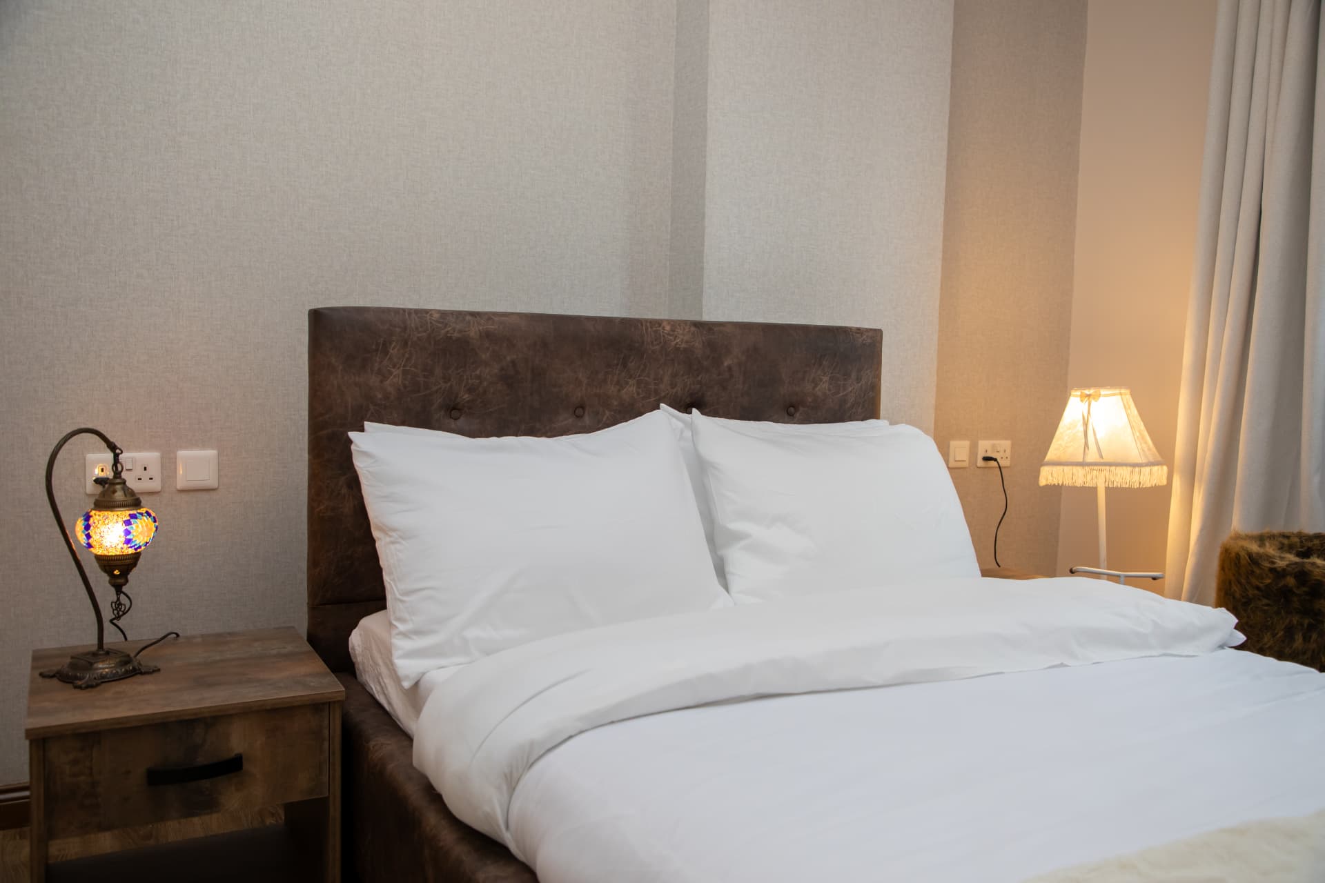 Bed made up with white linens and lit bedside lamps