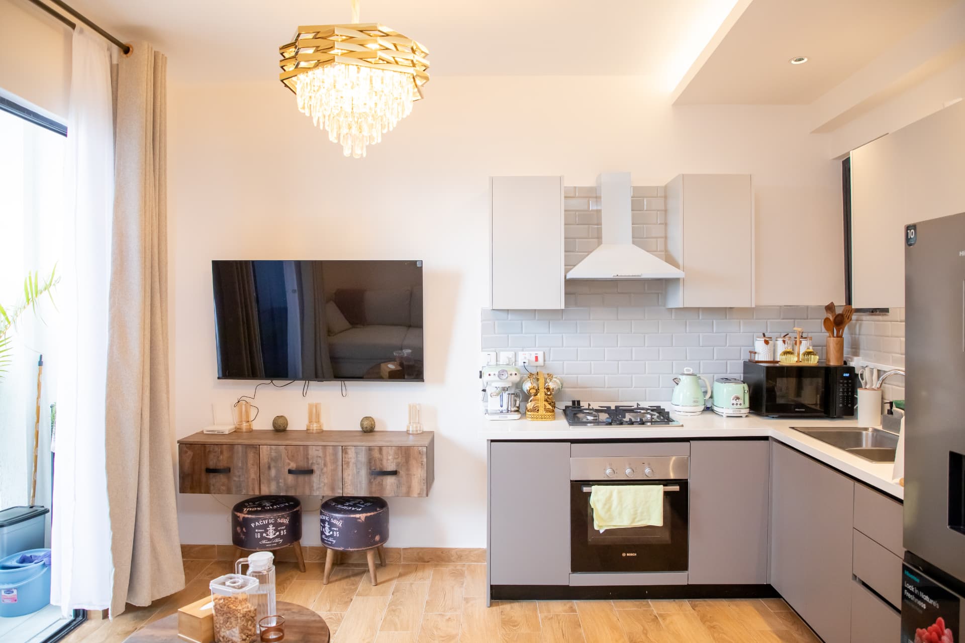 Open-plan living room with gold chandelier, TV wall and kitchen